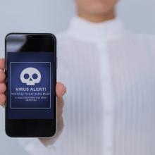 Una mano ense&ntilde;a un m&oacute;vil en cuya pantalla aparece una alerta de virus.